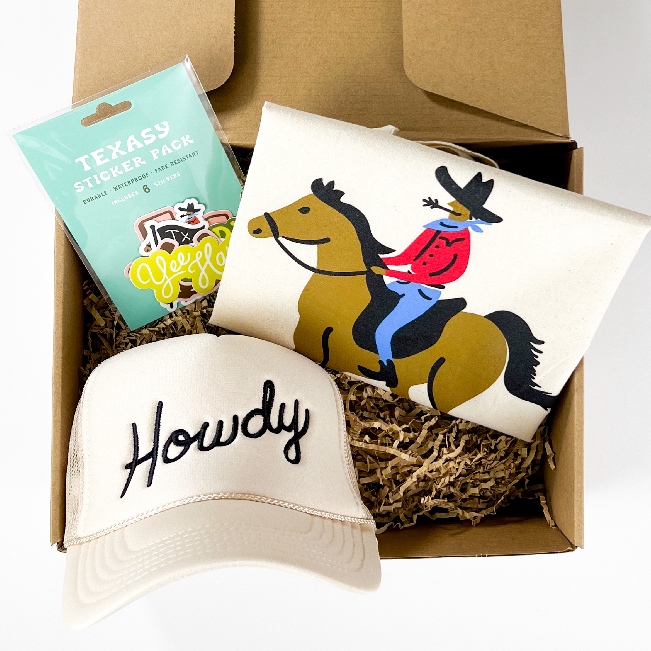 A Texasy gift box that includes a 'Howdy' cap, a cowboy tote bag, and a 6-pack of Texasy stickers.