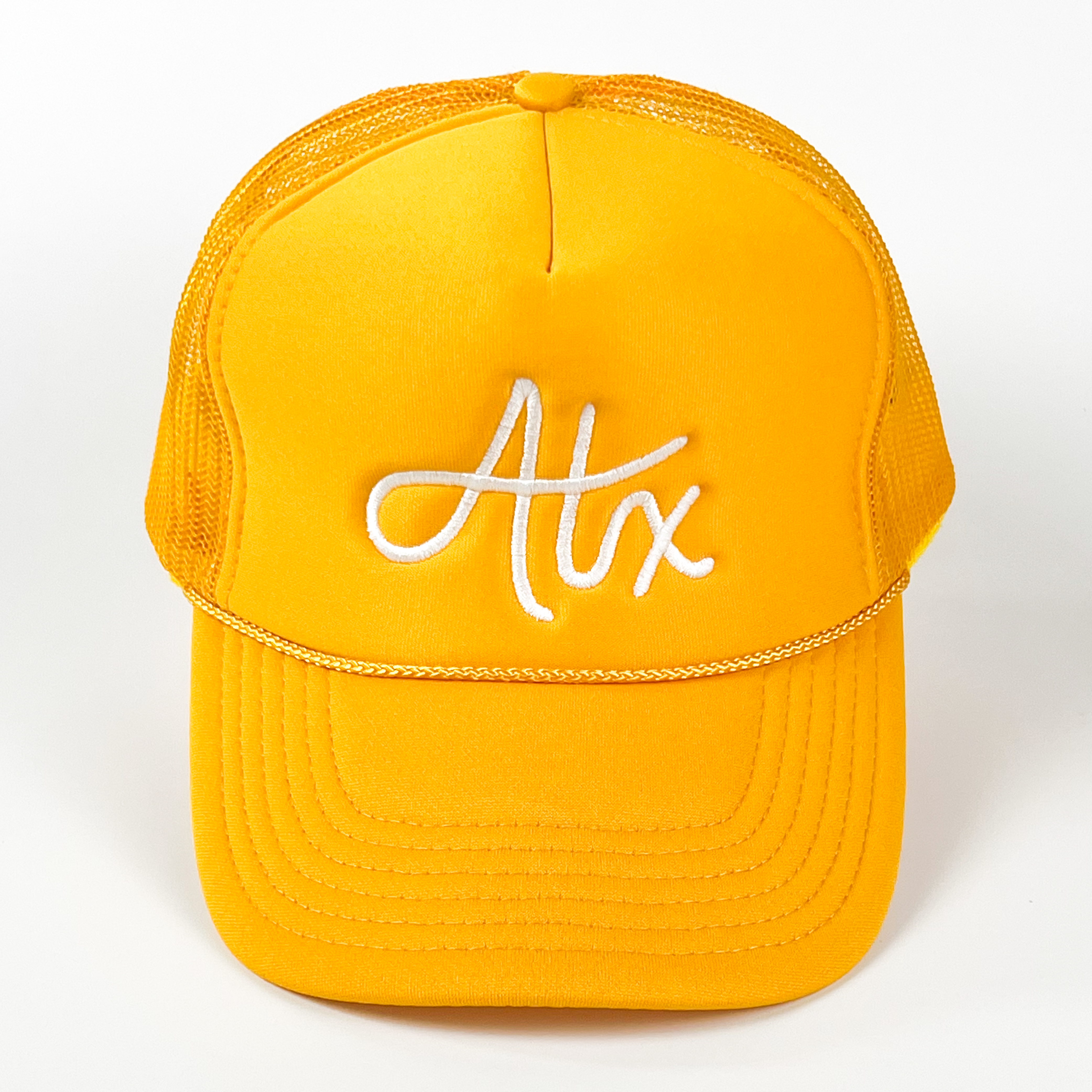 A yellow trucker cap with 'ATX' embroidered in a white thread.